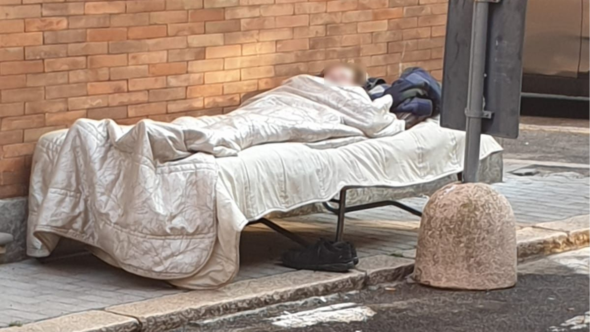 Donna senza dimora dorme da giorni su un letto all’aperto nel centro storico di Piacenza
