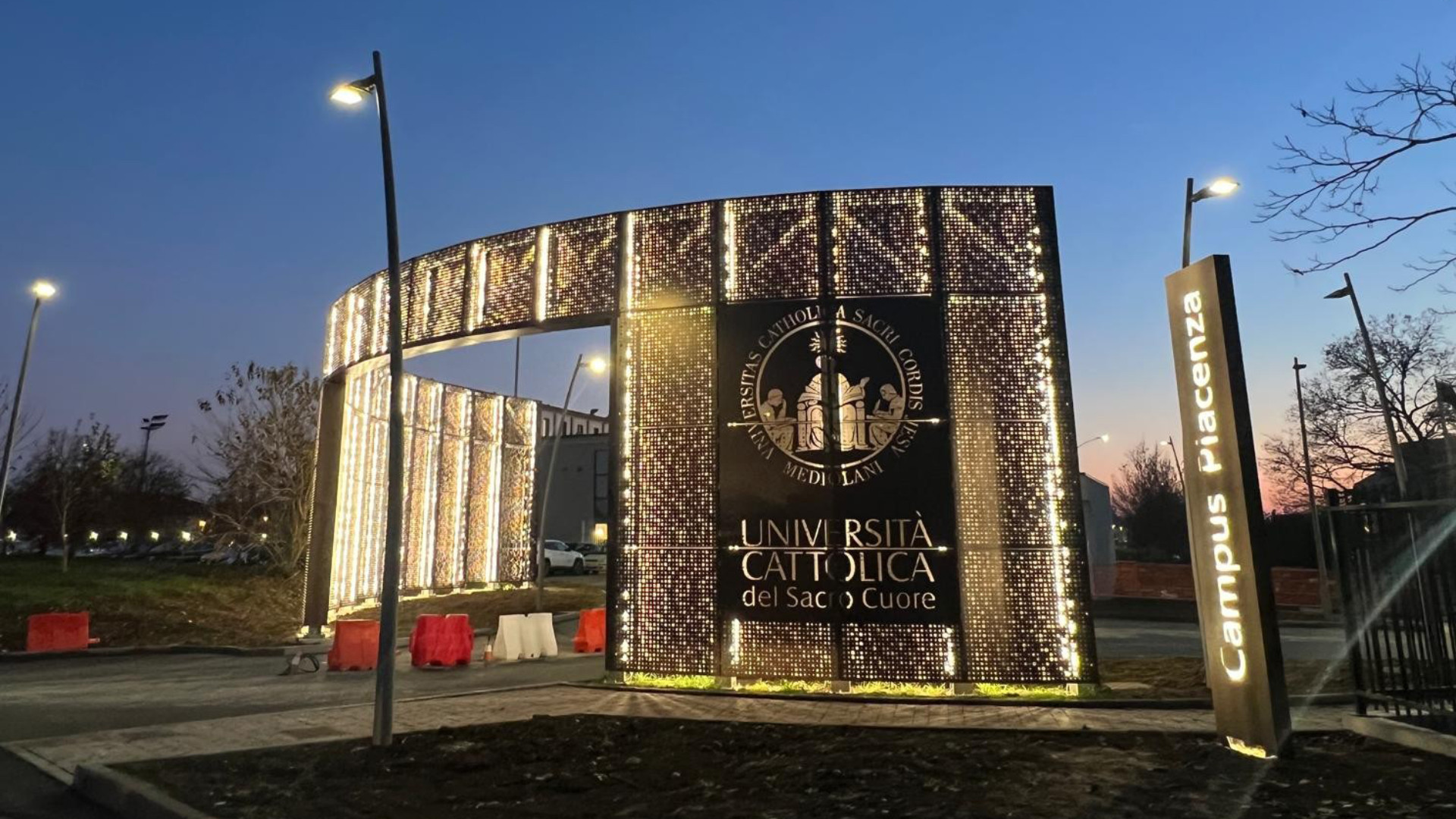 Il grande portale illuminato la sera che porta il marchio dell'Università Cattolica